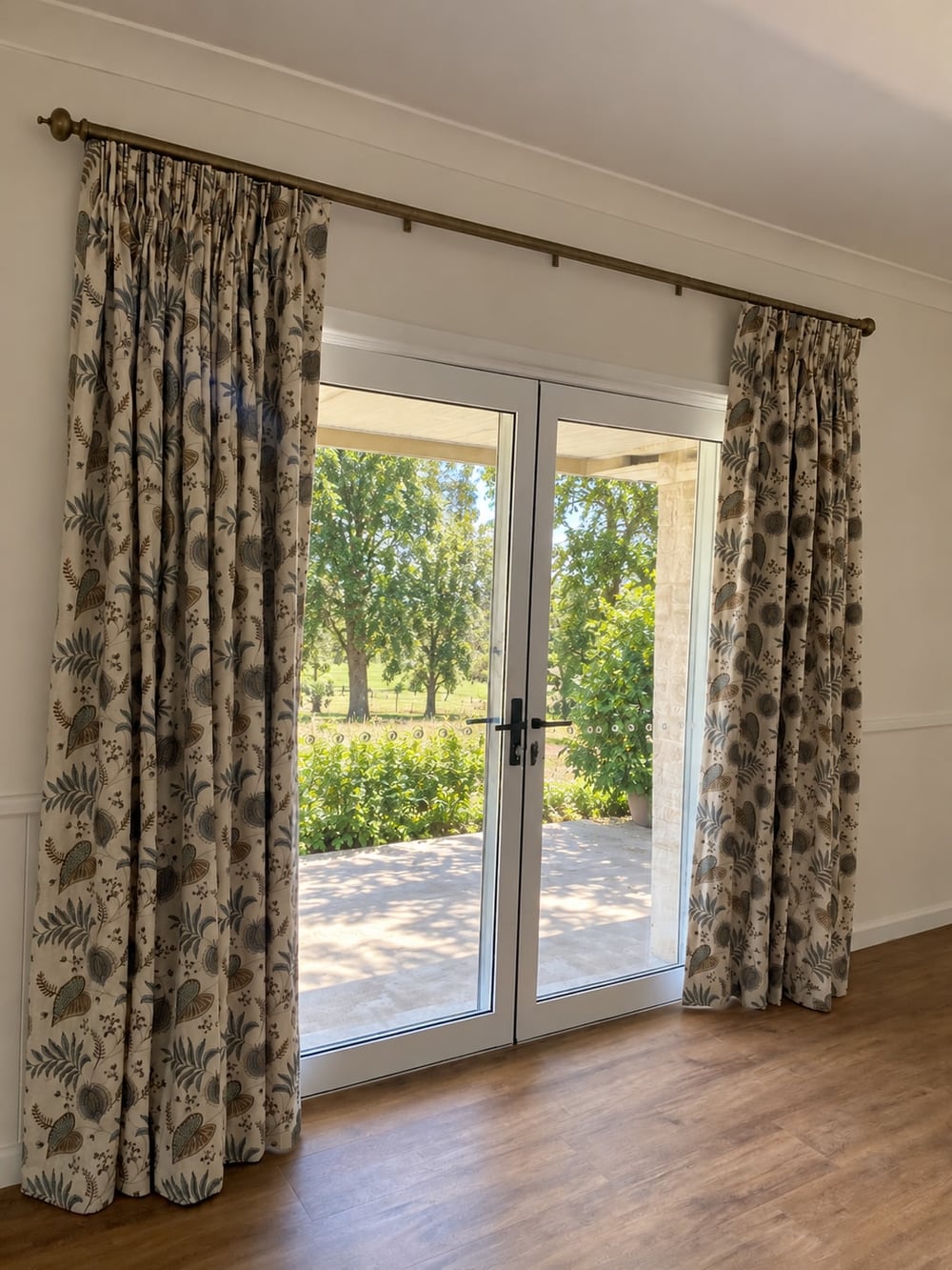 Floral pencil-pleat curtains on a brass rod framing white French doors