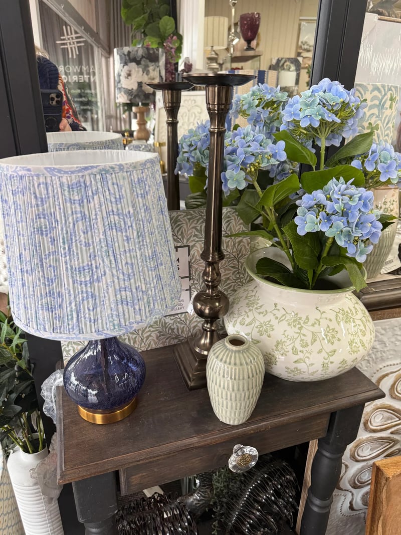 Blue patterned lamp, candlestick and hydrangeas on a dark timber table