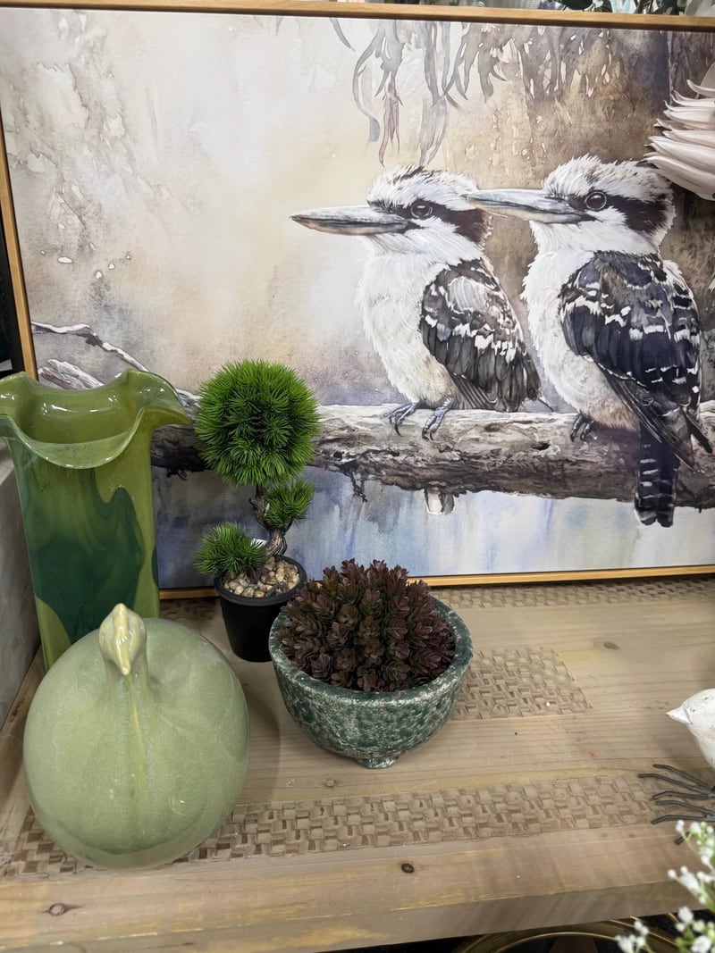 Green glass vase, ceramic bird and succulent in front of a kookaburra painting