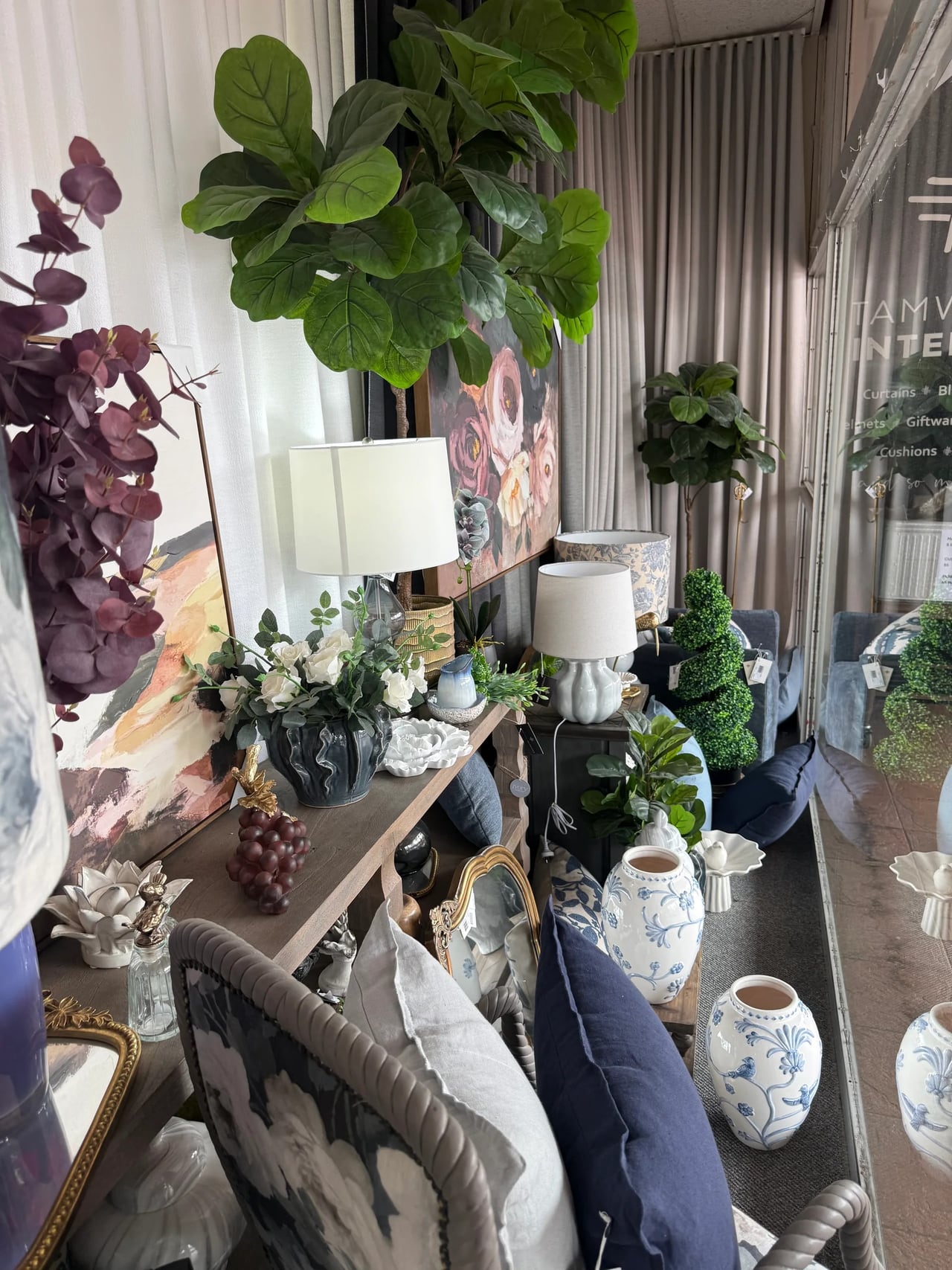 Tamworth Interiors showroom corner with lamps, vases, a chair and the shop name on the window